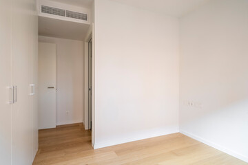 The image showcases a modern and minimalistic empty room with wooden flooring, white walls, and a white door, giving a sense of space and simplicity.
