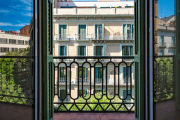 A close-up view from a balcony, focusing on a black wrought-iron railing with a clear sight of a neighboring building's classic architectural features, conveying elegance in Barcelona Spain