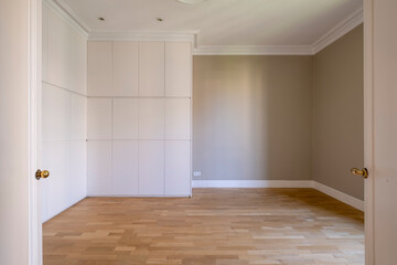 An empty room featuring light wooden flooring, white built-in storage cabinets, and softly colored walls, offering a blank canvas for interior design and decoration.