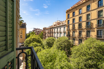 Daytime view of urban buildings adorned with balconies and surrounded by green leafy trees under a...