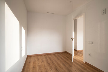 This image shows an empty room with a wooden floor and an open door, with sunlight streaming through, casting shadows and creating a warm and inviting atmosphere in the space.