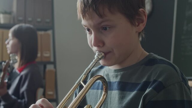 Tilt up shot of schoolchild playing trumpet at music lesson in classroom, girl with guitar in background