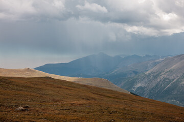Rain from the overhead storm clouds descends upon the distant mountains as viewed from atop Trail Ridge Road in Rocky Mountain National Park, Colorado in late August