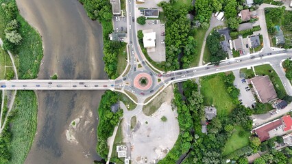 Aerial view of a roundabout with a bridge crossing a river surrounded by greenery in a suburban area © Wirestock