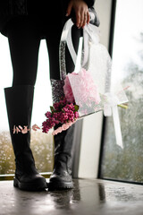 Cute young woman holding a transparent gift bag at her feet, covered with decorative raindrops with an autumn composition of flowers