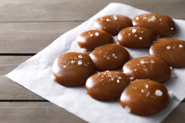 Tasty caramel candies and salt on wooden table, closeup