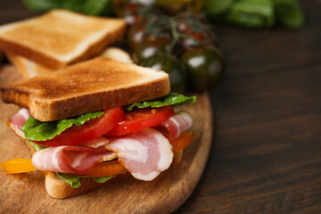 Tasty sandwich with bacon and tomato on wooden table, closeup. Space for text