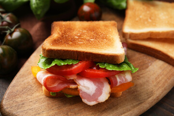 Tasty sandwich with bacon and tomato on wooden table, closeup