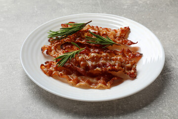 Slices of tasty fried bacon and rosemary on light grey table