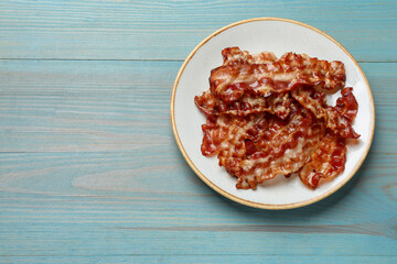 Slices of tasty fried bacon on light blue wooden table, top view. Space for text