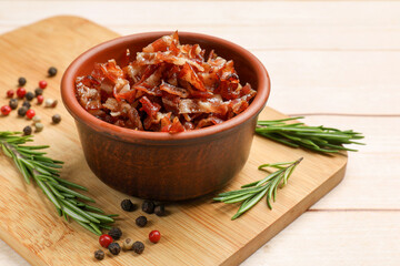 Pieces of tasty fried bacon in bowl and spices on wooden table, closeup