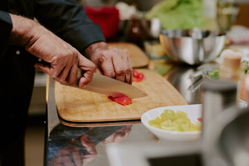 Unrecognizable chef hands cutting red bell pepper on wooden cutting board