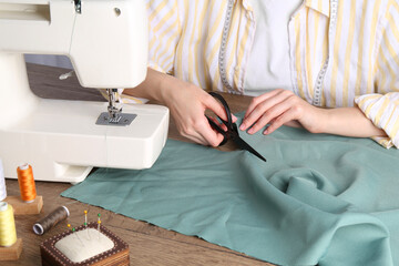 Seamstress cutting fabric at wooden table indoors, closeup