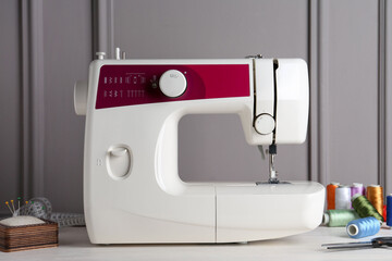 Sewing machine and craft accessories on white wooden table near gray wall