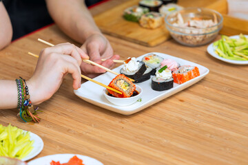 Close up of female hands holding chopsticks and eating sushi rolls.