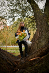 Young pretty woman in glasses is standing on a magnificent sprawling tree and holding a huge bouquet