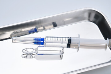 Syringes with needles and an ampoule in a stainless steel medical tray.