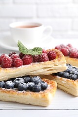 Tasty puff pastries with berries and tea on white wooden table, closeup