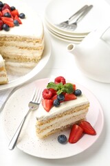 Tasty sponge cake with fresh berries and mint served on white table