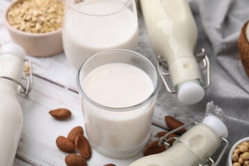 Different types of vegan milk and ingredients on white wooden table, closeup