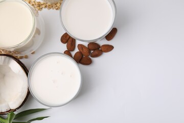 Different types of vegan milk and ingredients on white table, flat lay. Space for text