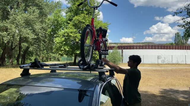 Teenage boy putting bicycle on car roof for trip. Car with roof bike rack transporting folding bike on the roof. Roof mount for carrying bikes.