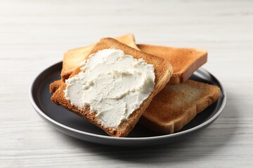 Delicious toasted bread slices with cream cheese on white wooden table