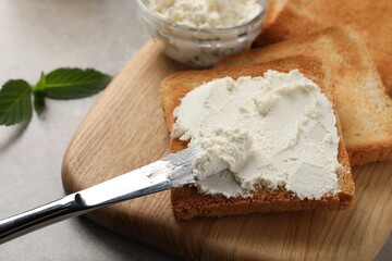 Delicious toasted bread slices with cream cheese and knife on grey table, closeup