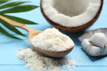 Fresh coconut flour in spoon, nut and palm leaf on light blue wooden table, closeup