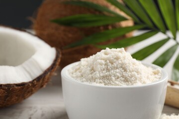 Fresh coconut flour in bowl, nuts and palm leaf on white table, closeup
