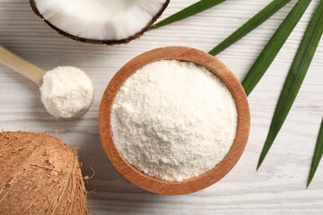 Fresh coconut flour in bowl, spoon, palm leaf and nut on white wooden table, flat lay
