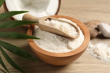 Fresh coconut flour in bowl, scoop, nut and palm leaf on wooden table, closeup