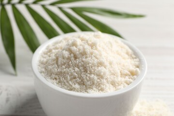 Fresh coconut flour in bowl and palm leaf on white table, closeup