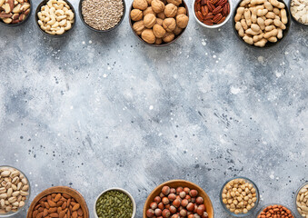 Mixed assorted nuts and seeds in various bowls on light kitchen table and space for text in the middle.Top view.