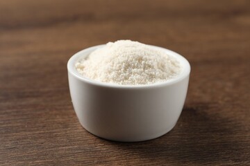 Organic coconut flour in bowl on wooden table, closeup
