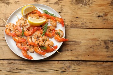 Skewers with delicious grilled shrimps served on wooden table, top view. Space for text