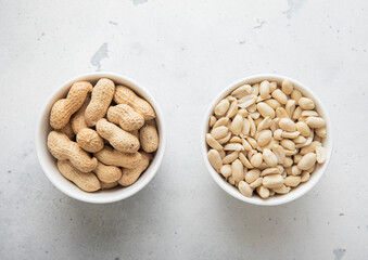 Bowls with whole and peeled healthy peanut nuts on light background.Top view.
