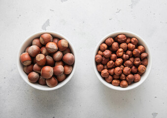 Bowls with whole and peeled healthy hazelnut nuts on light background.Top view.