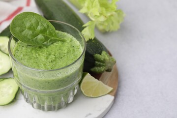 Tasty green smoothie in glass, lime and vegetables on light table, closeup. Space for text