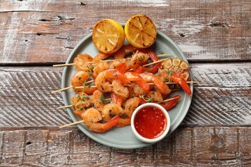 Delicious grilled shrimp skewers served with sauce and lemon on wooden table, top view