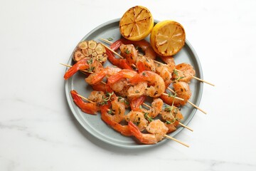 Skewers with delicious grilled shrimps, lemon and garlic on white marble table, top view