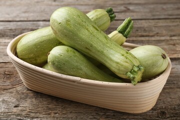 Raw green zucchinis in bowl on wooden table