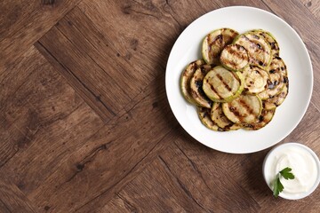 Tasty grilled courgette slices with sauce on wooden table, flat lay. Space for text