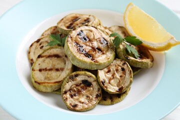 Tasty grilled zucchini slices with lemon and parsley on white table, closeup
