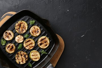 Tasty grilled zucchini slices with parsley in frying pan on grey textured table, top view. Space for text