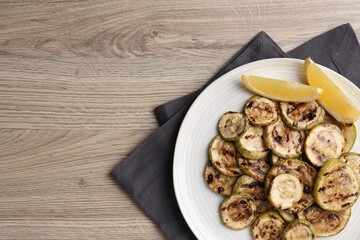 Tasty grilled courgette slices with lemon on wooden table, top view. Space for text