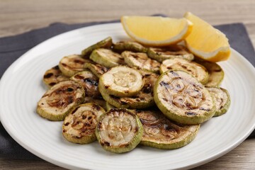 Tasty grilled courgette slices with lemon on wooden table, closeup