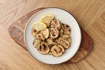 Tasty grilled courgette slices with lemon on wooden table, top view
