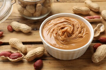 Tasty peanut butter in bowl and groundnuts on wooden table