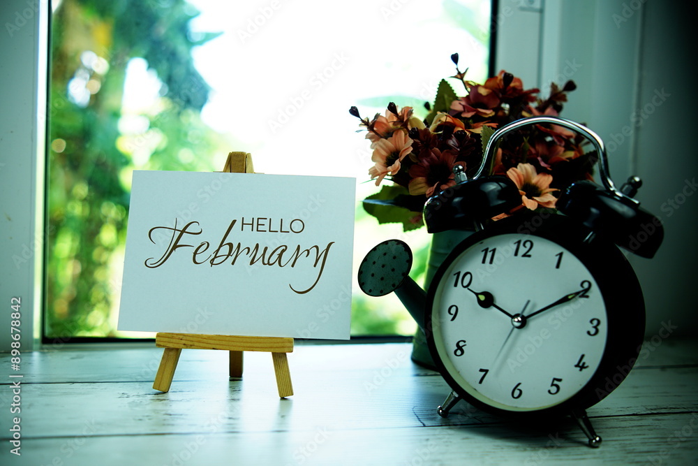 Poster hello february text on paper card with easel and alarm clock in the window background